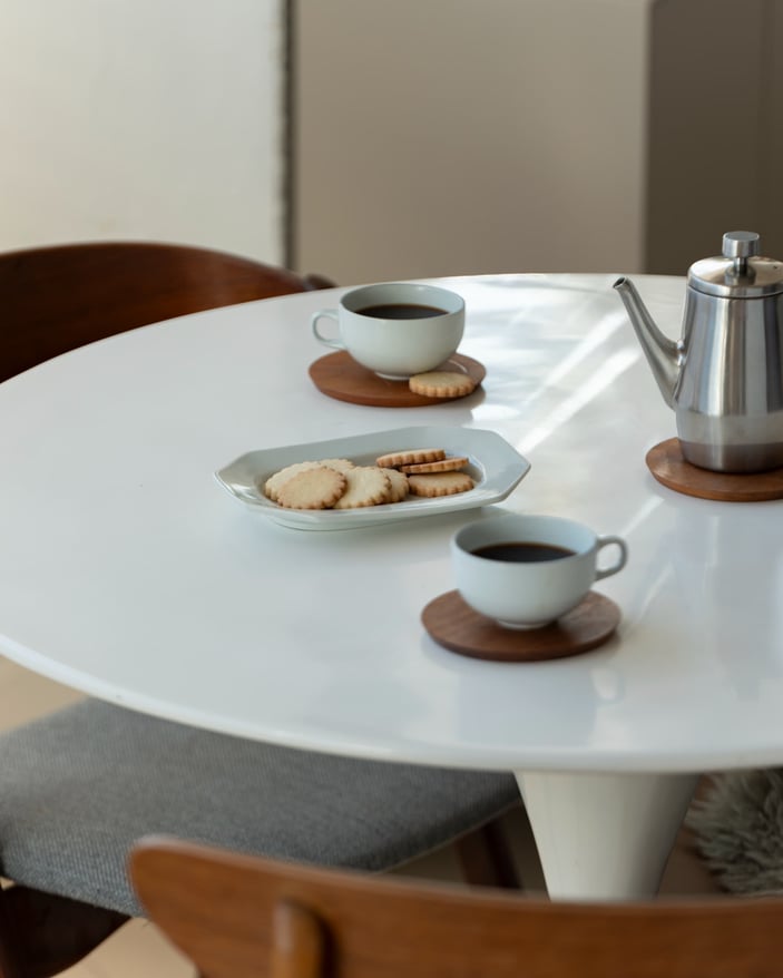 白いダイニングテーブルの上に置かれたコーヒーカップとクッキー、柔らかい朝の自然光が回る落ち着いたシーン