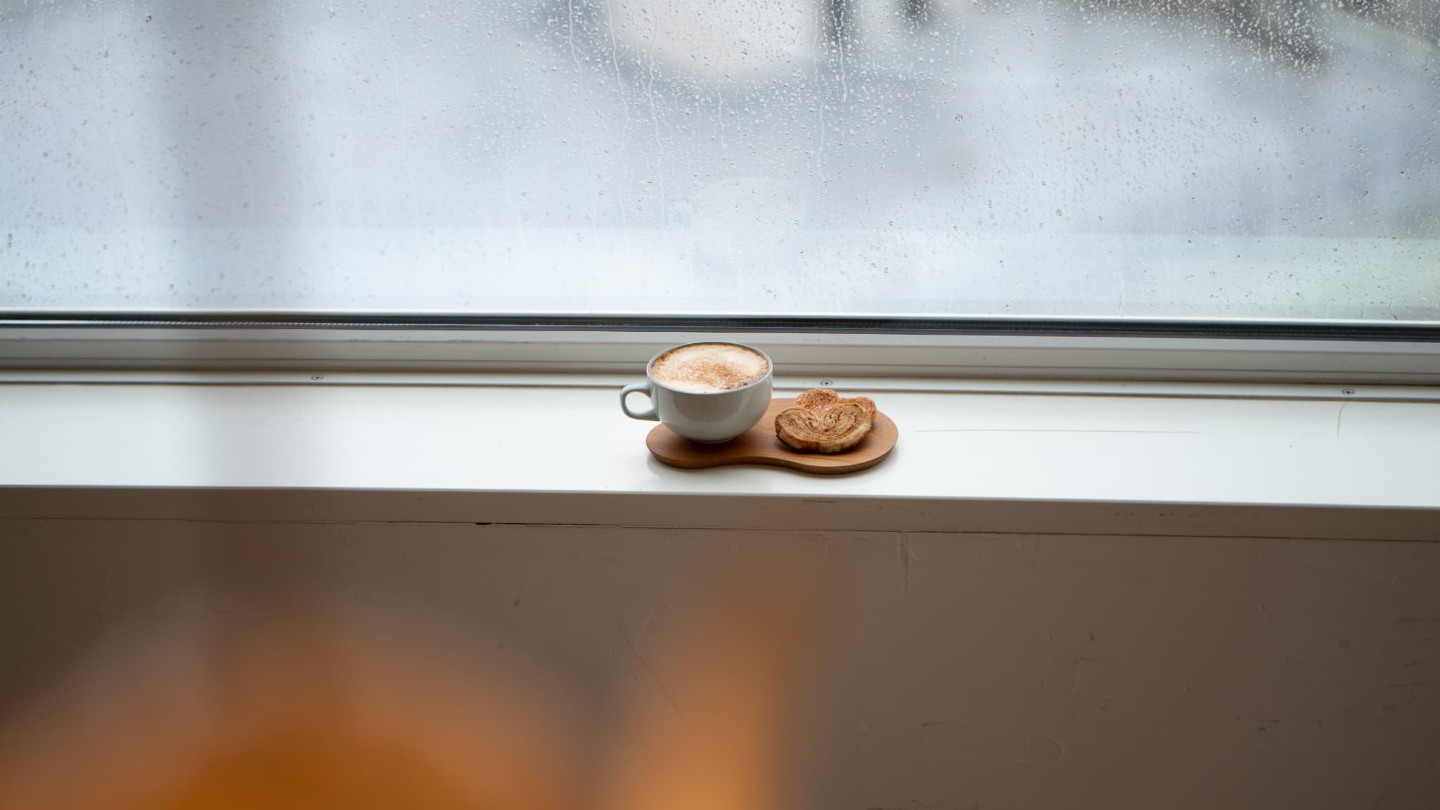 雨の日の窓辺に置かれたカフェオレと焼き菓子